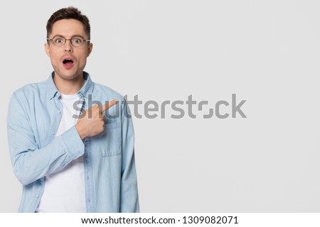 Shocked stunned young man nerd pointing finger aside at blank copy space advertising unbelievable presentation, astonished surprised guy looking at camera isolated on white grey studio background