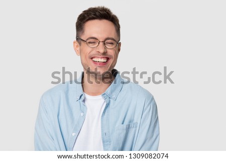 Happy man wearing glasses laughing at funny hilarious silly joke, young guy with cheerful face smiling chuckling giggling isolated on white grey studio blank background, laughter and humor concept