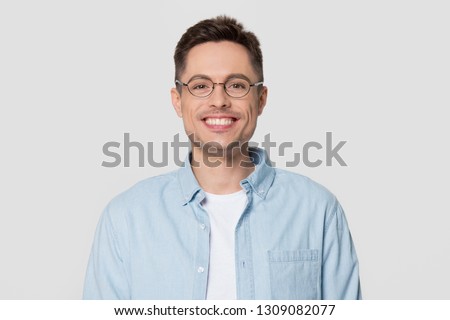 Smiling young man wearing shirt and glasses looking at camera, millennial guy nerd isolated on white grey studio blank background, funny male student geek in spectacles with happy face portrait