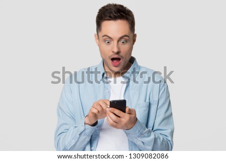 Surprised guy holding cellphone looking at phone shocked by unexpected  social media news, astonished young man amazed stunned by mobile online content isolated on white grey blank studio background Royalty-Free Stock Photo #1309082086