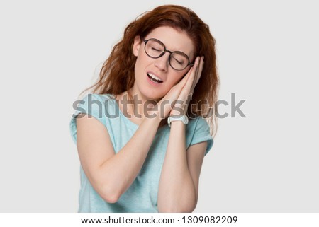 Young peaceful redhead woman resting on hands pretending sleeping isolated on white grey studio background, calm serene red-haired girl yawning standing asleep with eyes closed, healthy sleep concept