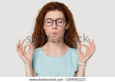 Stressed redhead woman meditating relieving managing stress doing yoga breathing exercises calming down, nervous red-haired lady exhaling self-soothing isolated on white grey studio blank background