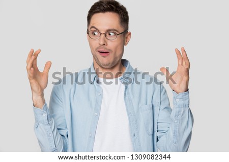 Funny shocked young man nerd looking at hands showing something huge, amazed confused guy in glasses bragging with large big size exaggerating gesture isolated on white grey blank studio background Royalty-Free Stock Photo #1309082344