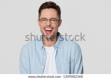 Funny guy nerd wearing glasses laughing at humorous hilarious silly joke looking at camera isolated on white grey blank background, happy cheerful young man chuckling giggling having fun portrait