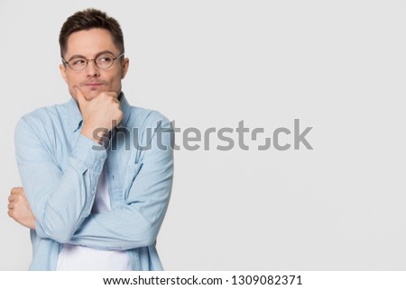 Thoughtful suspicious young man looking aside at copy space feeling skeptic doubtful, distrustful sly cunning guy thinking holding hand on chin isolated on grey white studio background Royalty-Free Stock Photo #1309082371