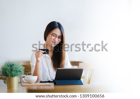 Young attractive happy Asian woman is using tablet for shopping and paying online by credit cards in her hand, online purchases content, commerce on the Internet shop background with white copy space.