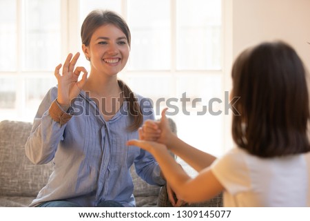 Mom baby sitter teacher or psychologist playing with little girl showing like ok signs by hands developing child motor concept, happy mother and kid daughter having fun,  sign language, deaf gesture
