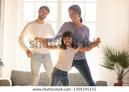 Happy funny family and cute little child daughter laughing dancing in modern living room, joyful parents mom dad with kid girl enjoying moving to music together, mortgage, fun and new home concept