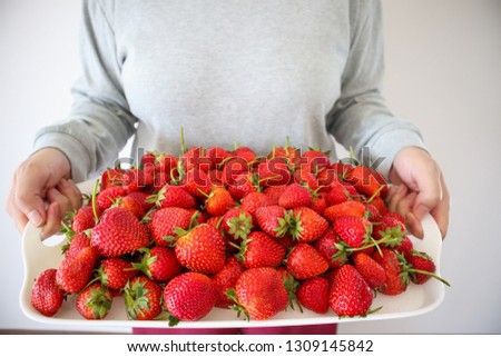 Woman hold white tray with red ripe strawberries