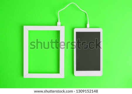 Flat lay of photo frame and blank screen digital tablet device connected with cable isolated on green background. Data transfer minimal creative concept.