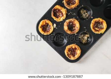 Traditional Portuguese egg tart dessert Pasteis Pastel de nata in black baking tray over white marble background. Flat lay, space