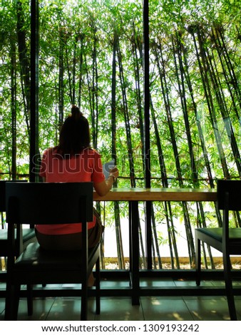 Alone woman living in the coffee shop and watching green leaves of bamboo tree.