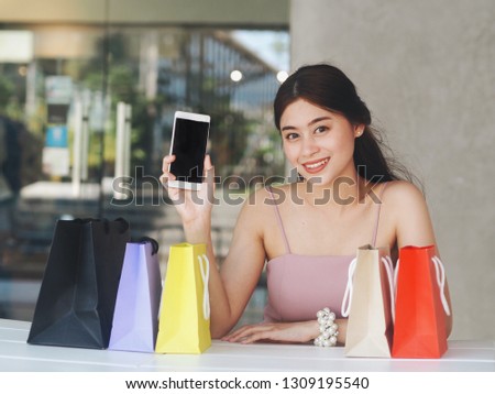 Happy Asian woman holding shopping bags by the shop.