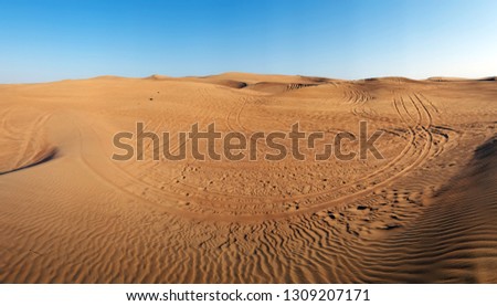 A picture in round angle of the sand desert in Dubai (UAE) with car tracks