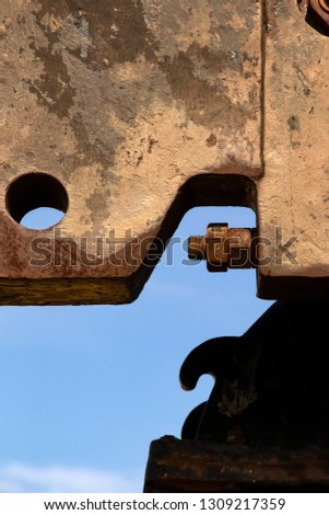 Grunge extreme close-up of rusted metal part of old pump jack with a bolt and nut and interesting shapes against a blue sky