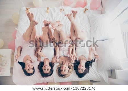 Top above high angle view of nice attractive charming cheerful cheery slim thin fit trendy girlfriends having fun lying on bed rising legs up showing v-sign in light white interior decorated house