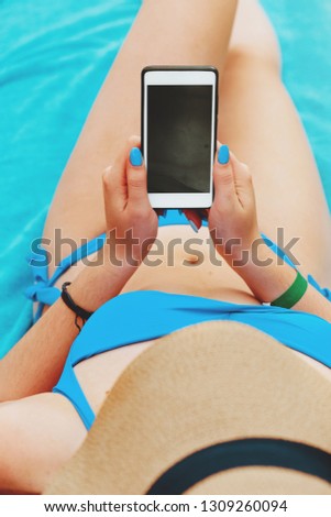 Young attractive woman on a beach by the sea, holding and using a smartphone to take pictures of the scenery. People travel technology outdoors.