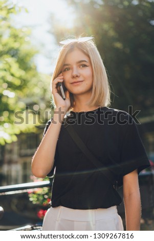 Happy smiling teenage girl calling to her friends using mobile phone and walking around the city streets, staying connected in every part of the world without limit, flare light and space for logo