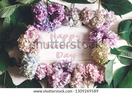 Happy Women's Day text sign in beautiful hydrangea flowers frame on rustic white wood, flat lay. Colorful border of hydrangea. Stylish floral greeting card. International womens day 8 march