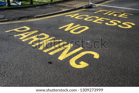 "No parking, Fire access" text sign with double yellow line on asphalt road.