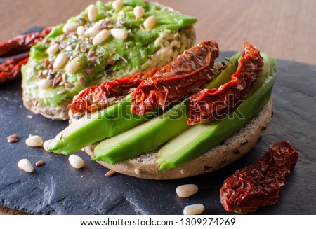 Avocado toast with dried tomatoes, pine nuts and flaxseeds on black stone desk. Close up. Angle view