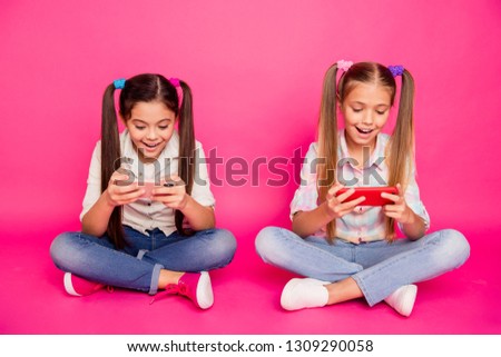 Close up photo two people little age she her girls hold hands arms new telephones sit floor addicted video games wear casual jeans denim checkered plaid shirts isolated pink rose vibrant background