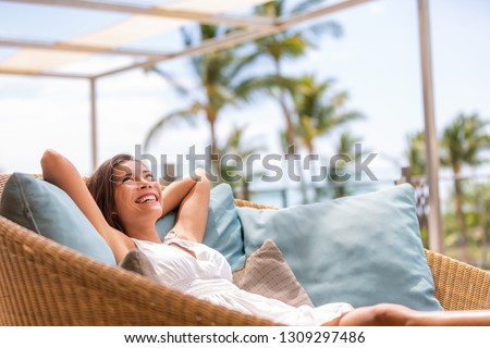 Luxury hotel home living woman relax enjoying sofa furniture of outdoor patio. Beautiful young multiracial Asian girl relaxing day dreaming for rich early retirement in getaway tropical house. Royalty-Free Stock Photo #1309297486
