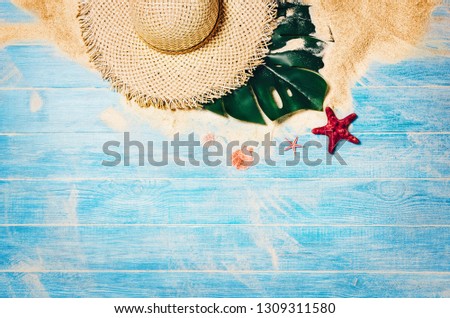Top view of sandy beach with blue marine planks frame and summer accessories. Background with copy space and visible sand and wood texture. Border composition