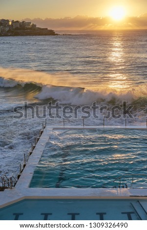Beach Scene: Waves crashing at sunrise on the famous ocean water swimming pools overlooking Bondi beach - Sydney, Australia.