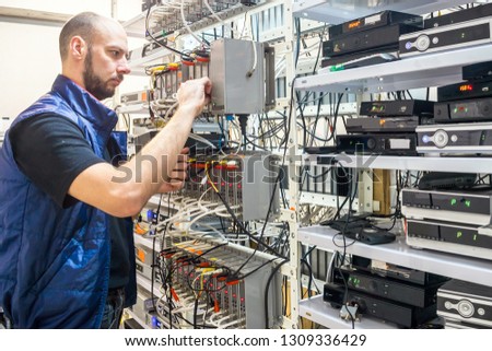 Specialist connects coaxial television wires in the rack of the TV station server room. Man switches  audio and video cable on the patch panel. Worker works on the control panel in the data center.