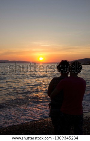 Back view of a couple silhouette hugging and watching sun on the beach