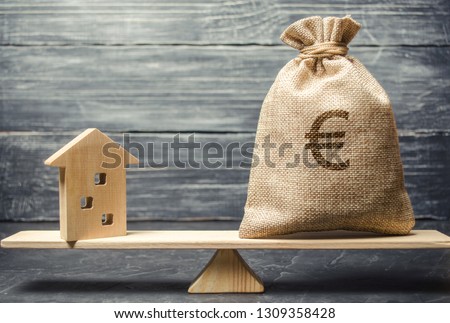A money bag and a wooden house on the scales. The concept of real estate purchase. Sale of property. Payment of the mortgage. Redemption of taxes. Tax refund. Legacy / Inheritance tax concept