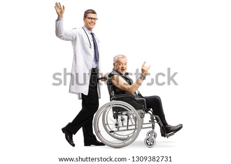 Full length shot of a young male doctor waving and pushing a mature male patient making a rock and roll hand sign in a wheelchair isolated on white background