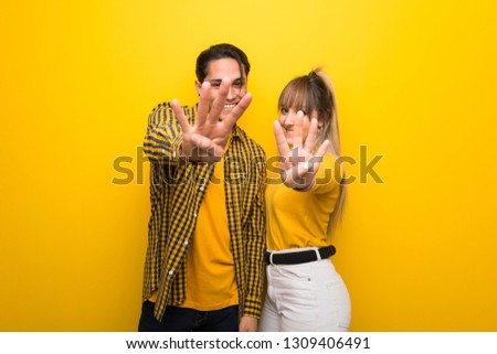 Young couple over vibrant yellow background happy and counting four with fingers