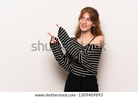 Young redhead woman over white wall pointing with the index finger and looking up