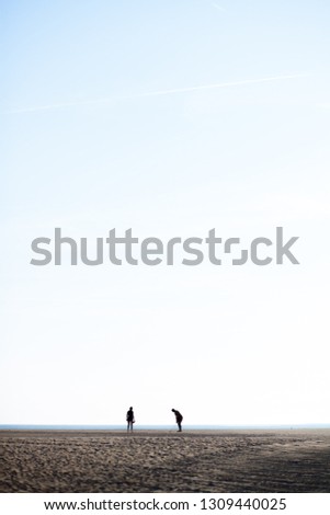 Couple in distance in silhouette playing golf on beach against bright sky
