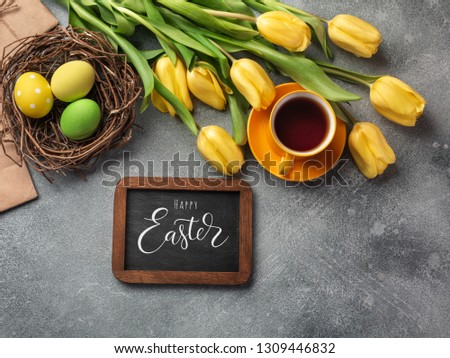 Easter background with blue, green eggs and a cup of tea in nest and yellow tulips. Top view with copy space