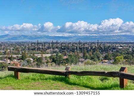 Bird eye view of Silicon Valley toward San Jose after cold winter storm with white snow-capped San Francisco Bay Area peaks of Diablo mountain range from green hill with wooden fence