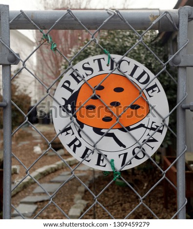 PESTICIDE FREE ZONE residential garden sign attached to chain link fence.