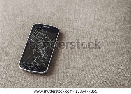 Black old cellphone with cracked screen on light cloth copy space background. Gadget repair and maintenance concept.
