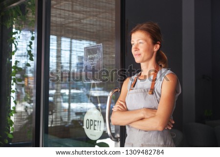 A female waitress, the owner of a cafe sits in the door of a cafe with a sign Open waiting for customers. Small business concept, cafes and restaurants
