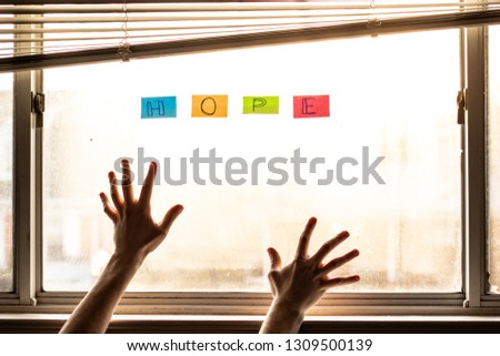 Hands reaching towards word hope on sunlit window
