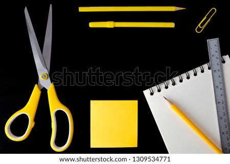 Yellow theme bright color school stationary supplies on black background.  Pencils ruler notepad sticky notes paper clip scissor top view with copy space