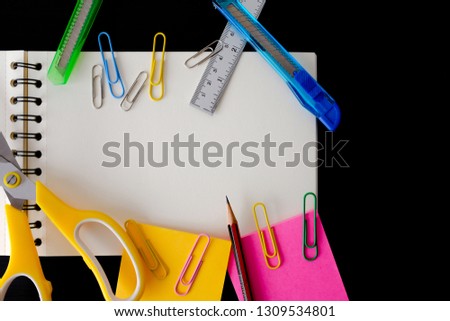 Bright multicolor school stationary supplies on black background.  Colored pencils ruler notepad sticky notes cutter paper clip scissor paper puncher top view with copy space