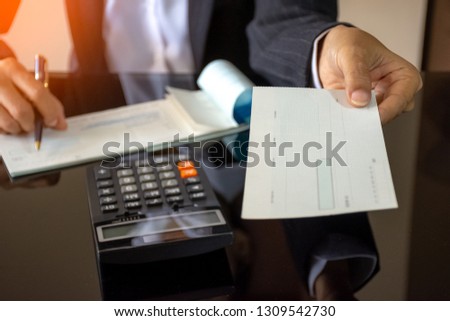 Businessperson hand holding and giving blank cheque to colleague or partnership with calculator on the desk at office. Bonus and Paycheck concept.