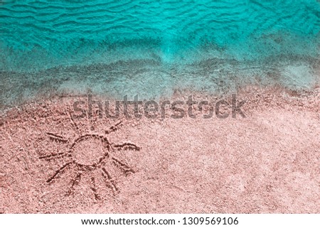 Sun is drawn on sandy beach on sea coast with clear azure blue water, on rest summer vacation. Top view, background close-up.