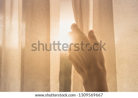 New day concept. Woman's hand opening window curtains early morning with natural light shining through. 