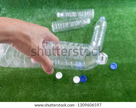 man hand holding recycled plastic water bottles on artificial grass