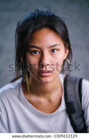 Close up head shot portrait of a young and attractive Chinese Asian girl in a white tee shirt. She is a young millennial teenager. 