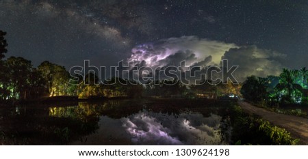 The photo was taken in the monsoon season while thunderstorms are lightening behind the clouds and it reflecting in the water of the field. at that same time the milky way is clearly visible.